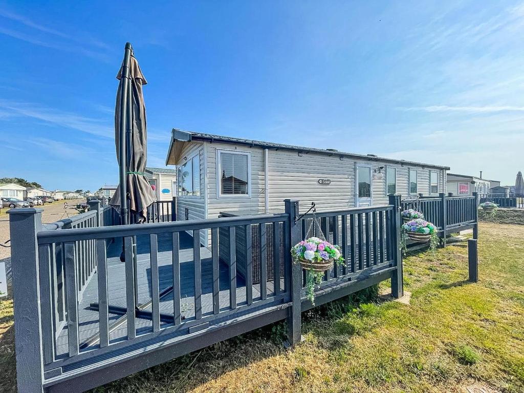 a house with a fence and an umbrella at Lovely Caravan With Decking Free Wifi At North Denes Caravan Park Ref 40145nd in Lowestoft