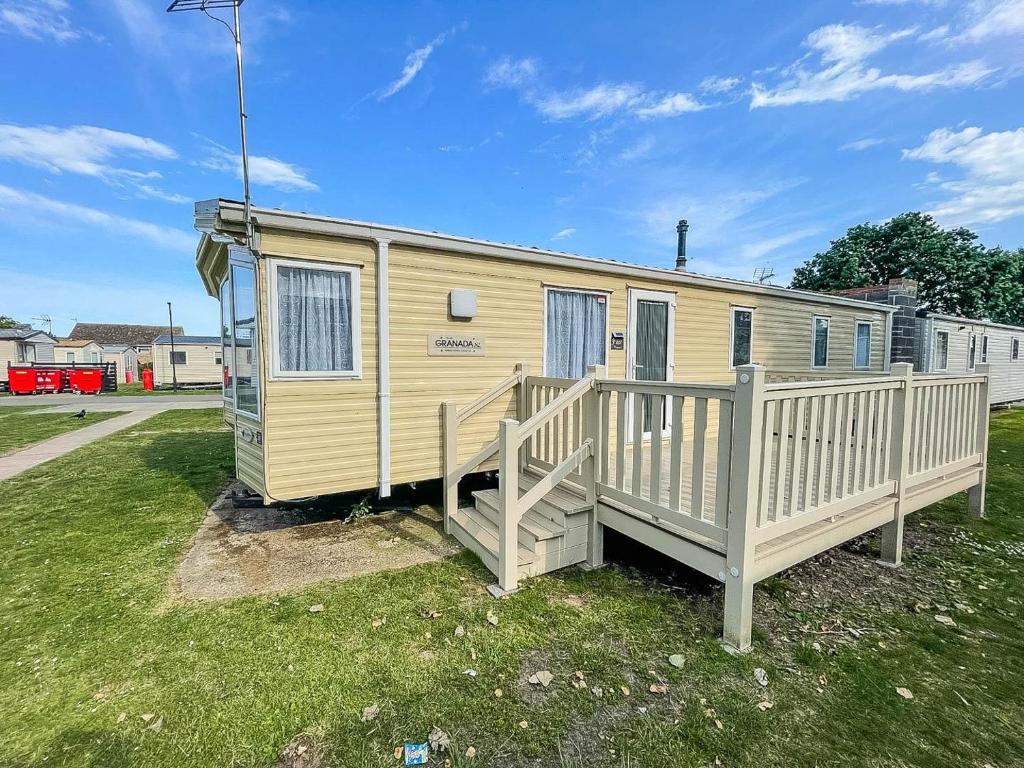 a yellow tiny house with a wooden porch at 8 Berth Caravan For Hire Near Clacton-on-sea In Essex Ref 26287e in Clacton-on-Sea