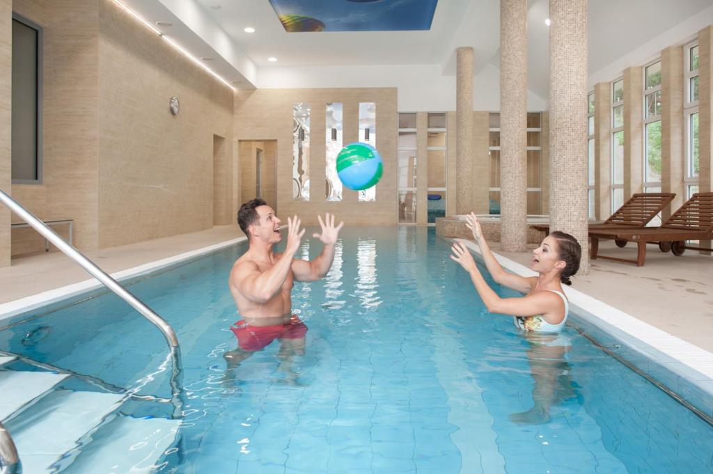 a man and a woman playing with a beach ball in a swimming pool at Hotel Cesarskie Ogrody in Świnoujście