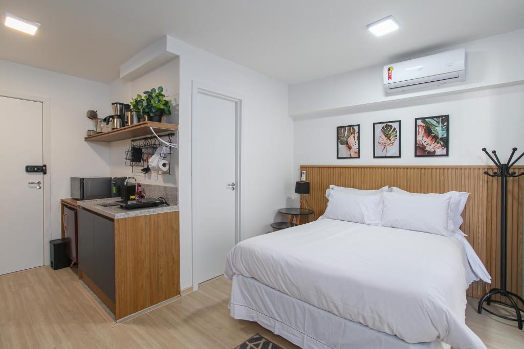 um quarto com uma cama branca e uma cozinha em MOL - Liberdade - Anora Spaces Residenciais em São Paulo