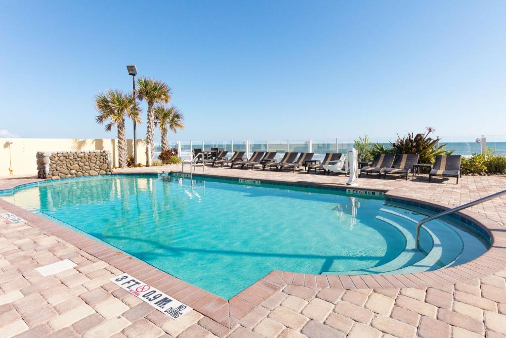 a swimming pool with chairs and the ocean in the background at Hampton Inn Daytona Beach/Beachfront in Daytona Beach