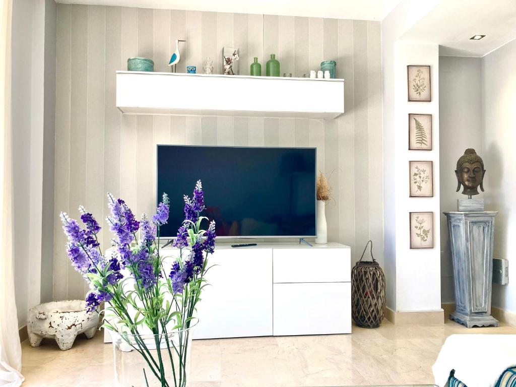 a living room with a tv and purple flowers at Golf&sea views townhouse. in San Roque