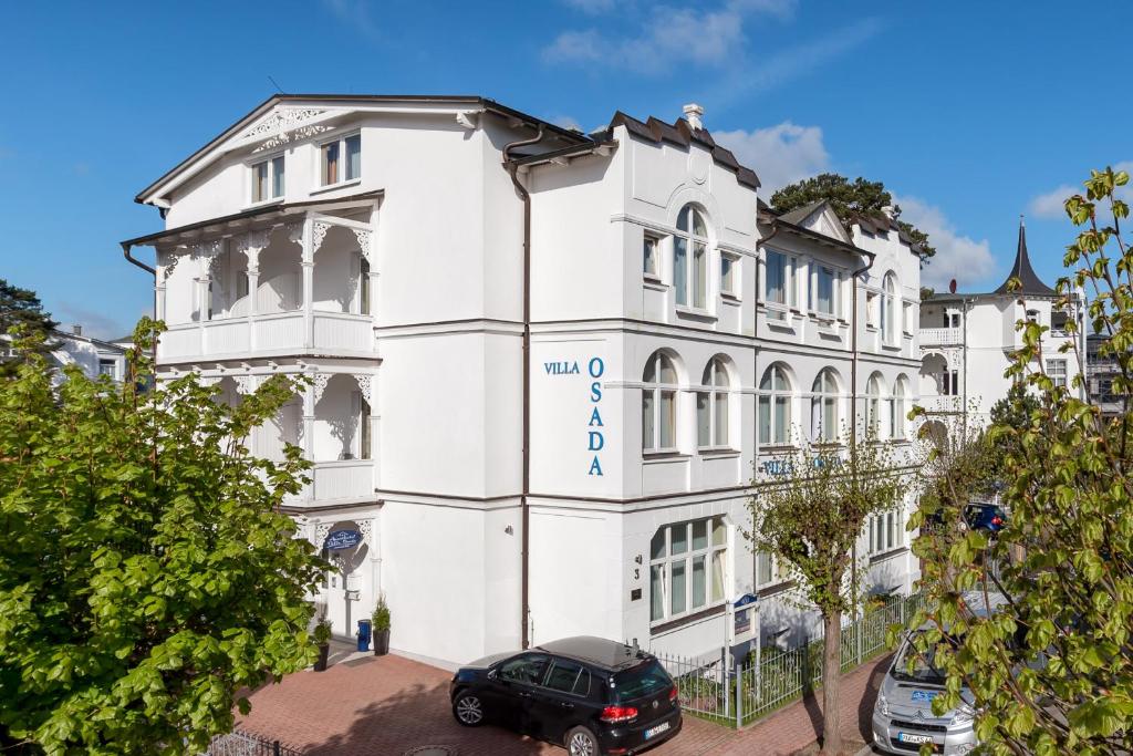 Un bâtiment blanc avec une voiture garée devant. dans l'établissement Villa Osada, à Binz