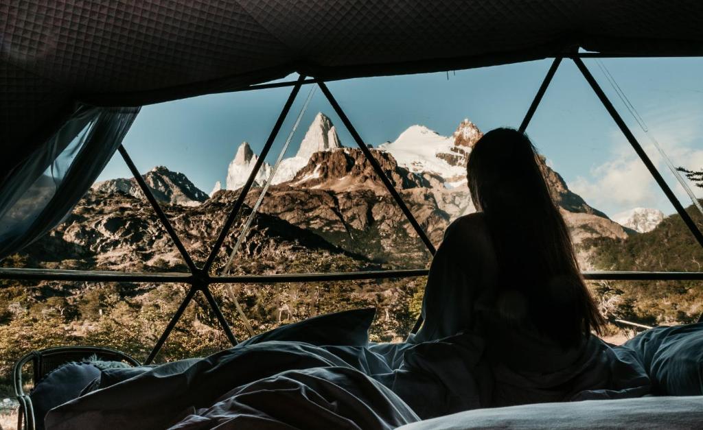 uma mulher sentada numa tenda com vista para as montanhas em Patagonia Eco Domes em El Chaltén
