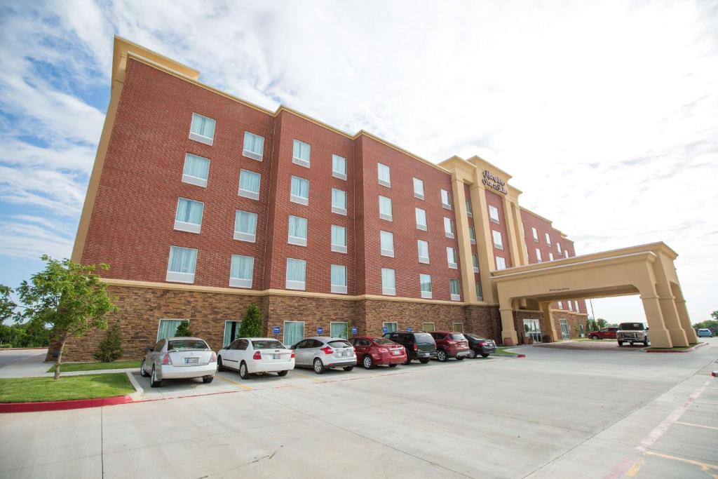 un gran edificio de ladrillo rojo con coches aparcados en un aparcamiento en Hampton Inn & Suites Oklahoma City Airport en Oklahoma City