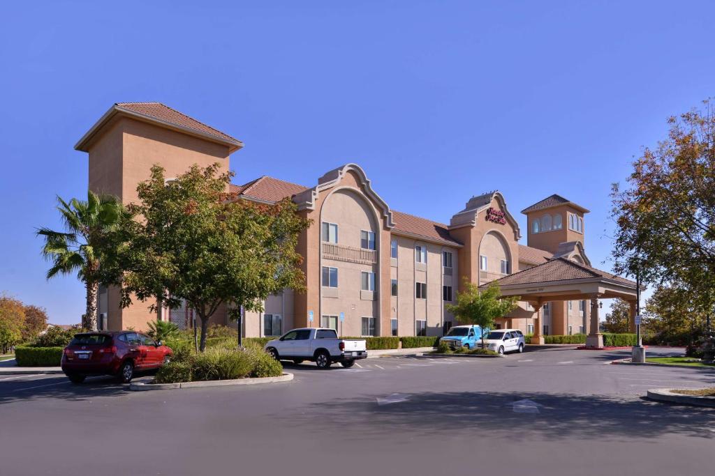 Hampton Inn & Suites Woodland-Sacramento Area في وودلاند: مبنى كبير به سيارات تقف في موقف للسيارات