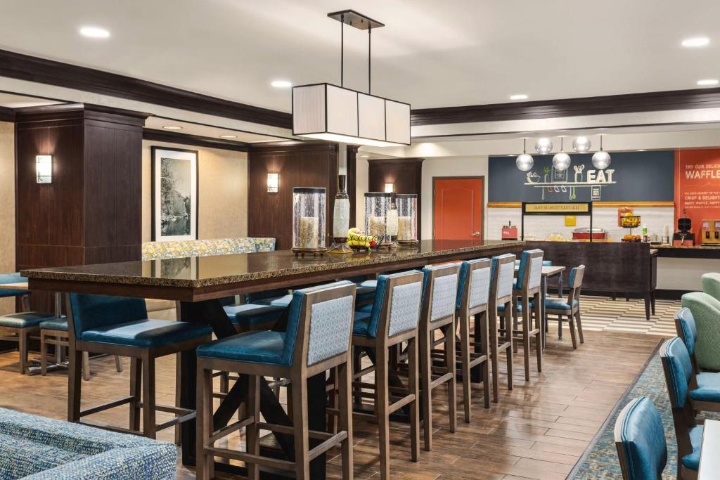 a restaurant with a long bar with blue chairs at Hampton Inn New Albany in New Albany