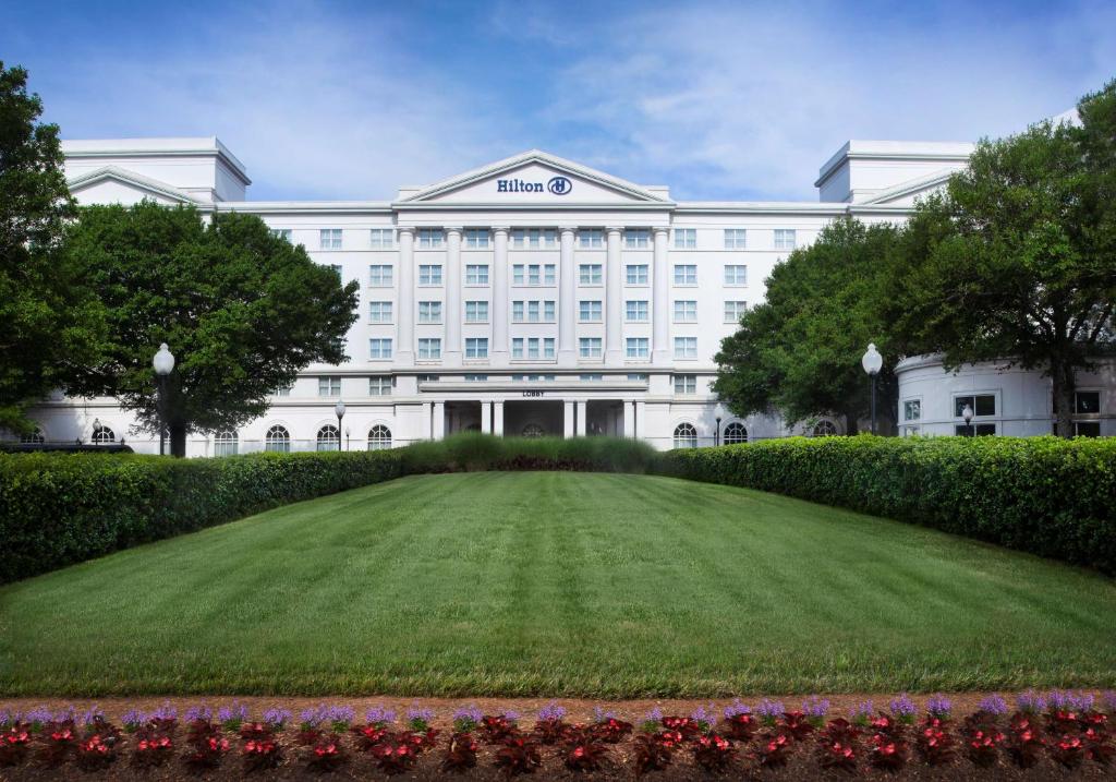 Hilton Atlanta/Marietta Hotel & Conference Center في ماريتا: مبنى أبيض كبير مع حديقة أمامه