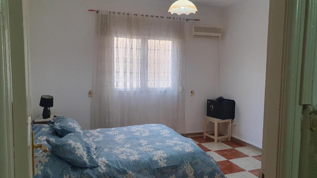 a bedroom with a bed with a blue comforter and a window at Villa 250 m2 terrasse plus Garage in Mostaganem