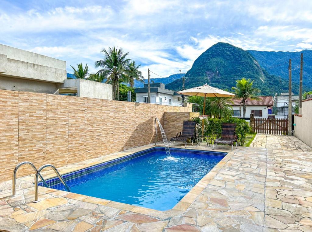 a swimming pool with two chairs and an umbrella at Otima casa com WiFi e churrasqueira em Bertioga SP in Bertioga