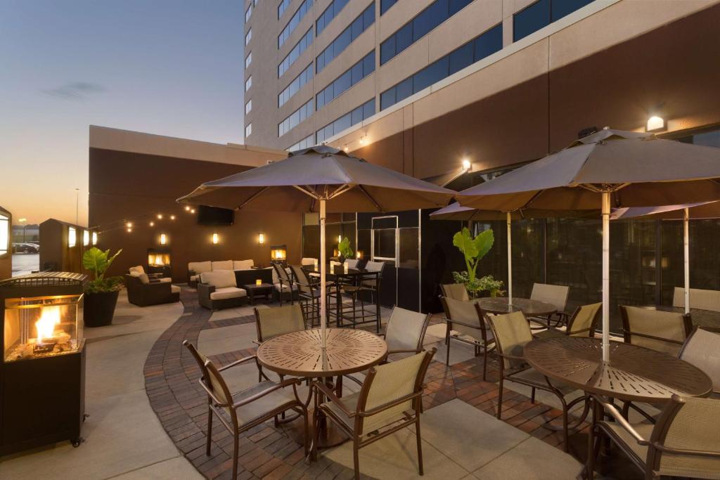 un patio al aire libre con mesas, sillas y sombrillas en Hilton Suites Chicago/Oakbrook Terrace, en Oakbrook Terrace