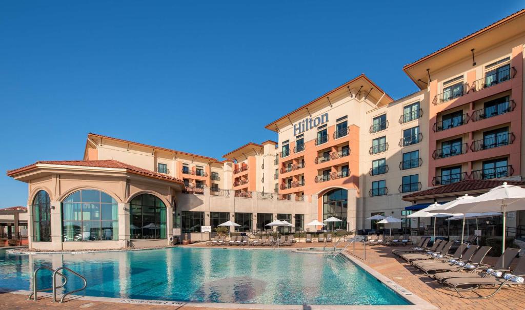 a pool in front of a hotel with chairs and umbrellas at Hilton Dallas/Rockwall Lakefront Hotel in Rockwall