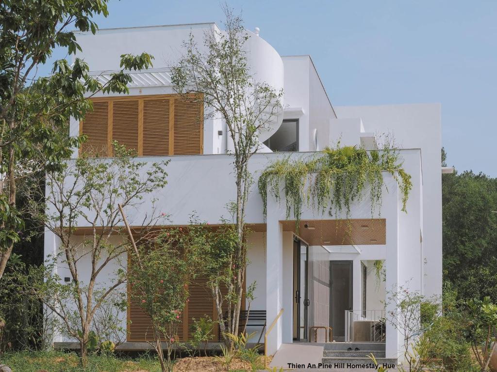 a white house with trees in front of it at Thien An Pine Hill Homestay Hue in Hue