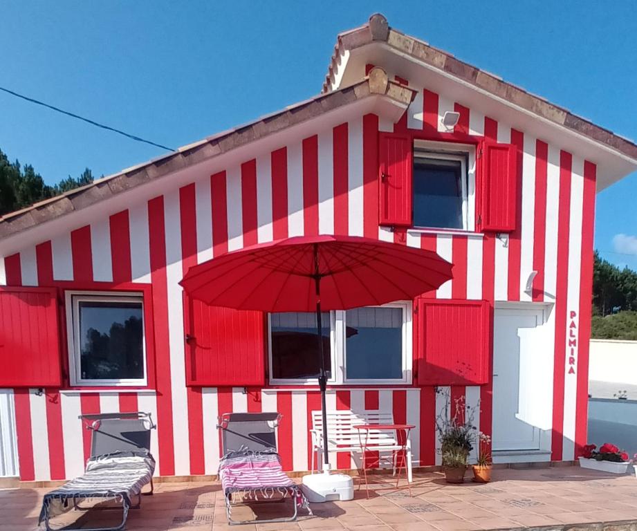 un edificio rosso e bianco con sedie e ombrellone di Casiña Palmira a Finisterre