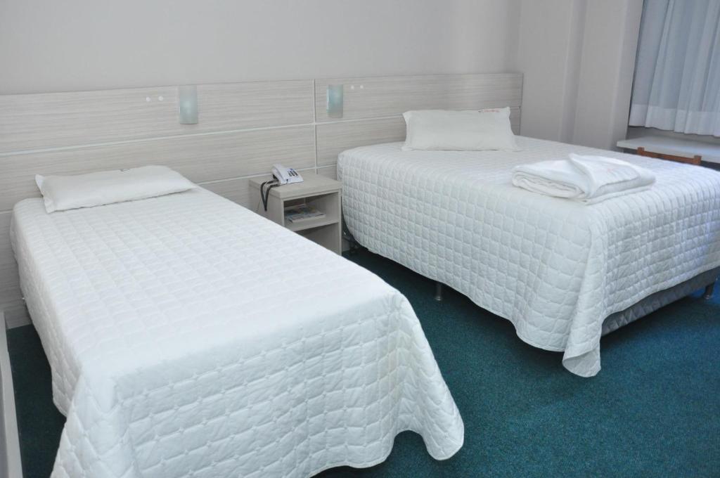 2 camas en una habitación de hotel con sábanas blancas en Rede Andrade San Martin, en Curitiba