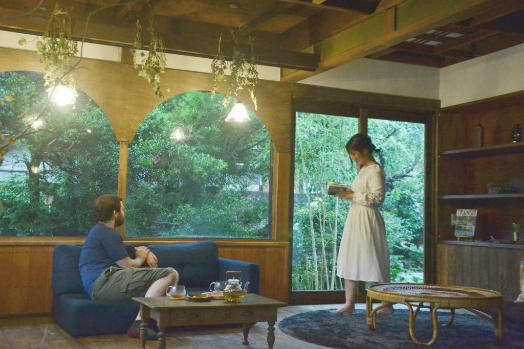 una mujer parada en una sala de estar hablando con un hombre en 野窓 Nomadノマド Tsuwano GuestHouse & Cafe Lounge en Tsuwano