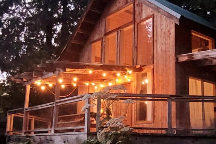 a house with lights on the front of it at Ocean Views & Sunset Beach Cabin with soaker tub & fire pit in Powell River