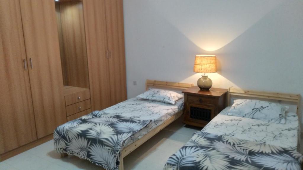 1 dormitorio con 2 camas y mesita de noche con lámpara en Baran Homestay, en Mascate