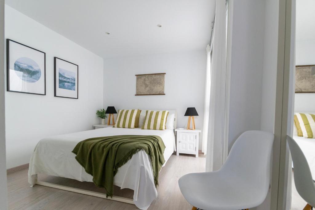 a white bedroom with a bed and a chair at Amplio apartamento recién reformado in La Playa de Arguineguín