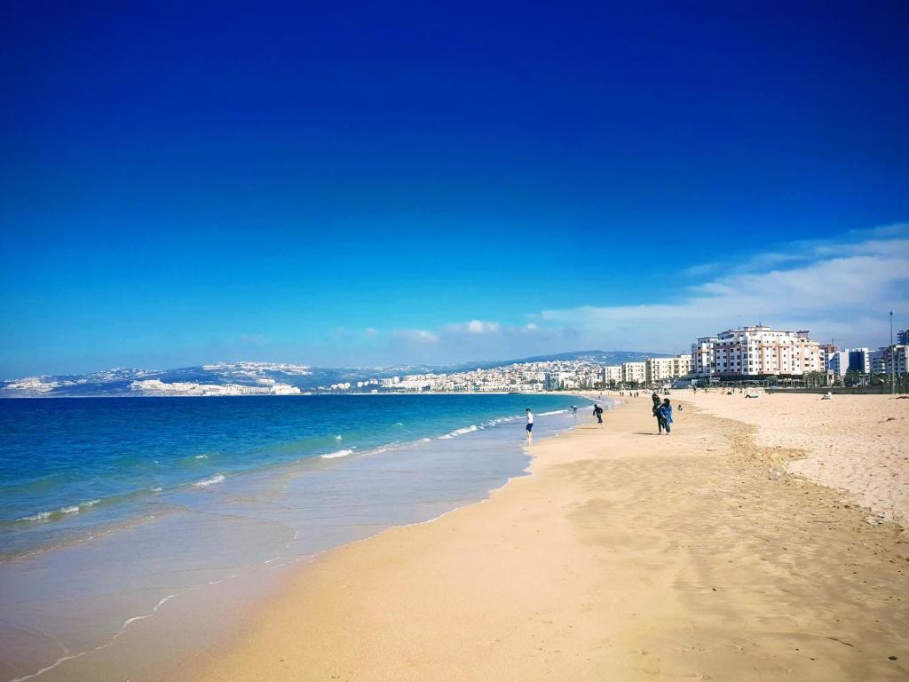 a beach with people walking on the sand and the ocean at Superbe Appartement Avec Cheminée in Tangier