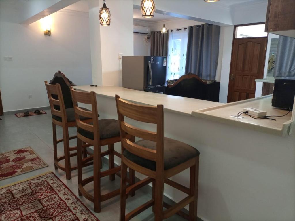 a kitchen with a bar with four wooden stools at NYALI LUXURY APARTMENT in Mombasa