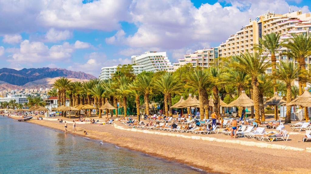 una playa con gente sentada en sillas y sombrillas en אופק במדבר - 2 חדרי אירוח מקסימים ונעימים קרוב לטיילת ולים, en Eilat