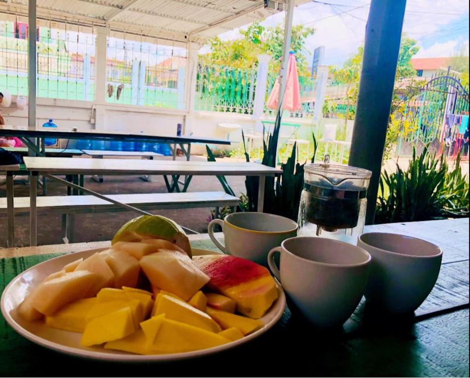 a plate of fruit on a table with cups at Vernice Backpacker Hostel in Vientiane