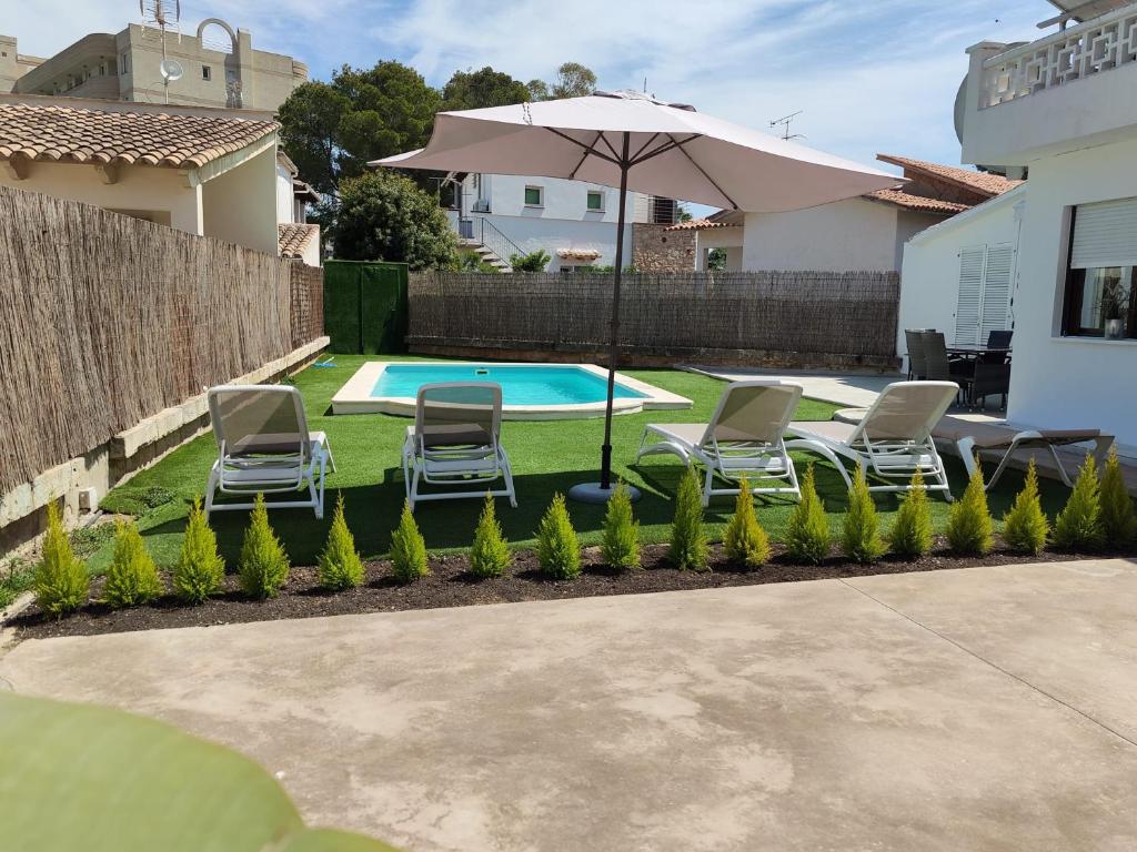 un patio trasero con piscina, sillas y sombrilla en VILLA BERNA, en Alcudia