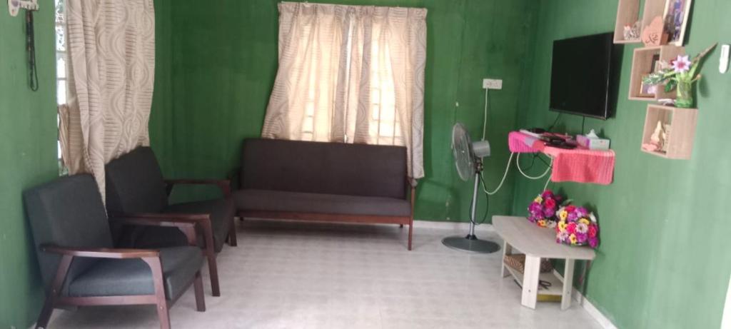 uma sala de estar com paredes verdes e um sofá e cadeiras em BB Bahau Homestay em Bahau