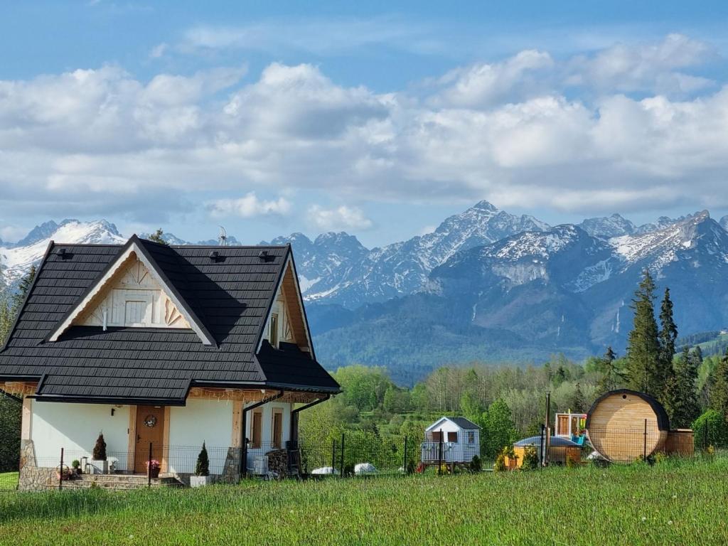 a house with a black roof with mountains in the background at W Sercu Tatr in Rzepiska
