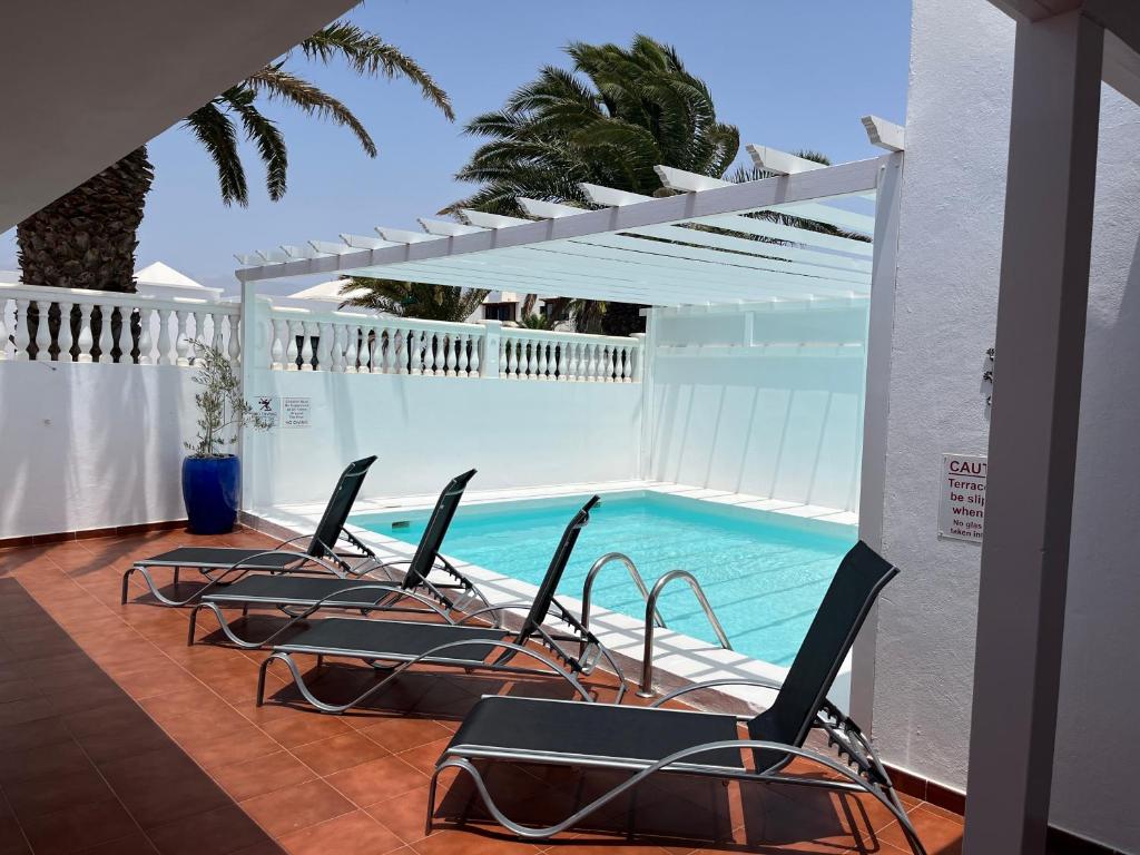 a group of chairs sitting on a patio with a swimming pool at Casa Costa Bella in Costa Teguise