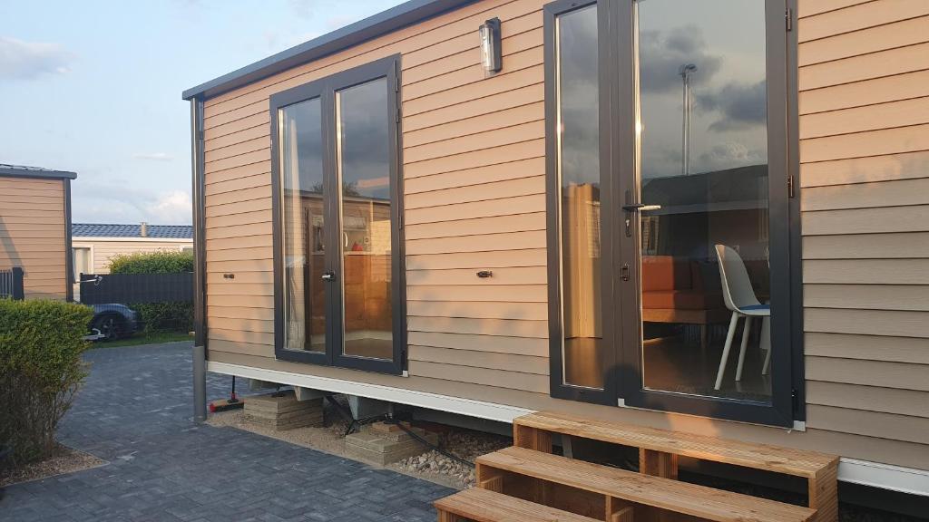 ein Haus mit Glasfenstern, einem Stuhl und einem Tisch in der Unterkunft Campingland Ostsee - Mobilheim 74Strandzauber NEU! in Schashagen