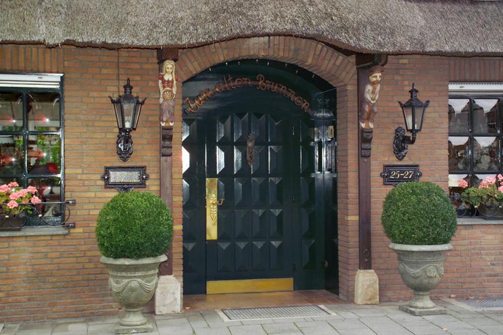 une porte noire sur un bâtiment en briques avec deux plantes dans l'établissement Hotel Zum Alten Brunnen, à Rheine