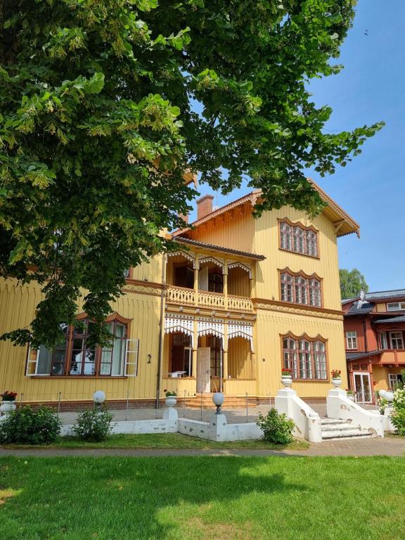 uma grande casa amarela com uma árvore em frente em Villa OLD POST em Juodkrantė