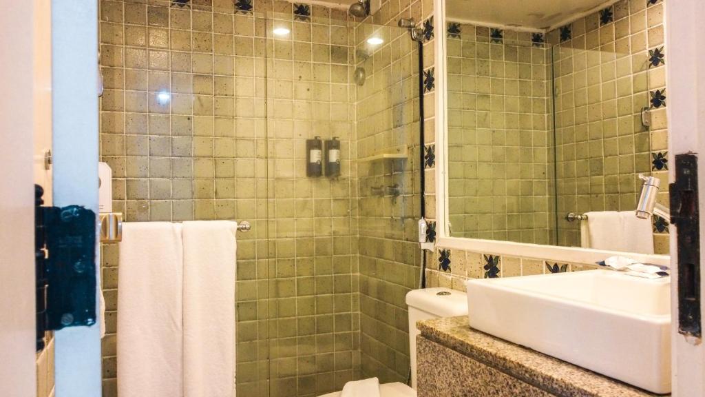 uma casa de banho com um lavatório e um chuveiro com um espelho. em Jatiuca Suítes Resort FLAT em Maceió