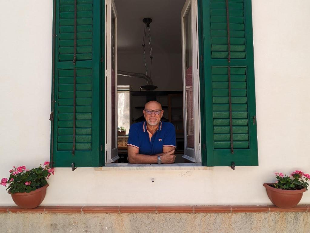 un hombre mirando por una ventana con persianas verdes en Casa Ficumora, en Módica