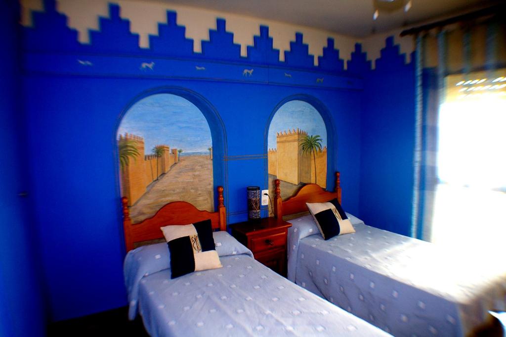 two beds in a room with blue walls at Pensión El Alamo in Lepe