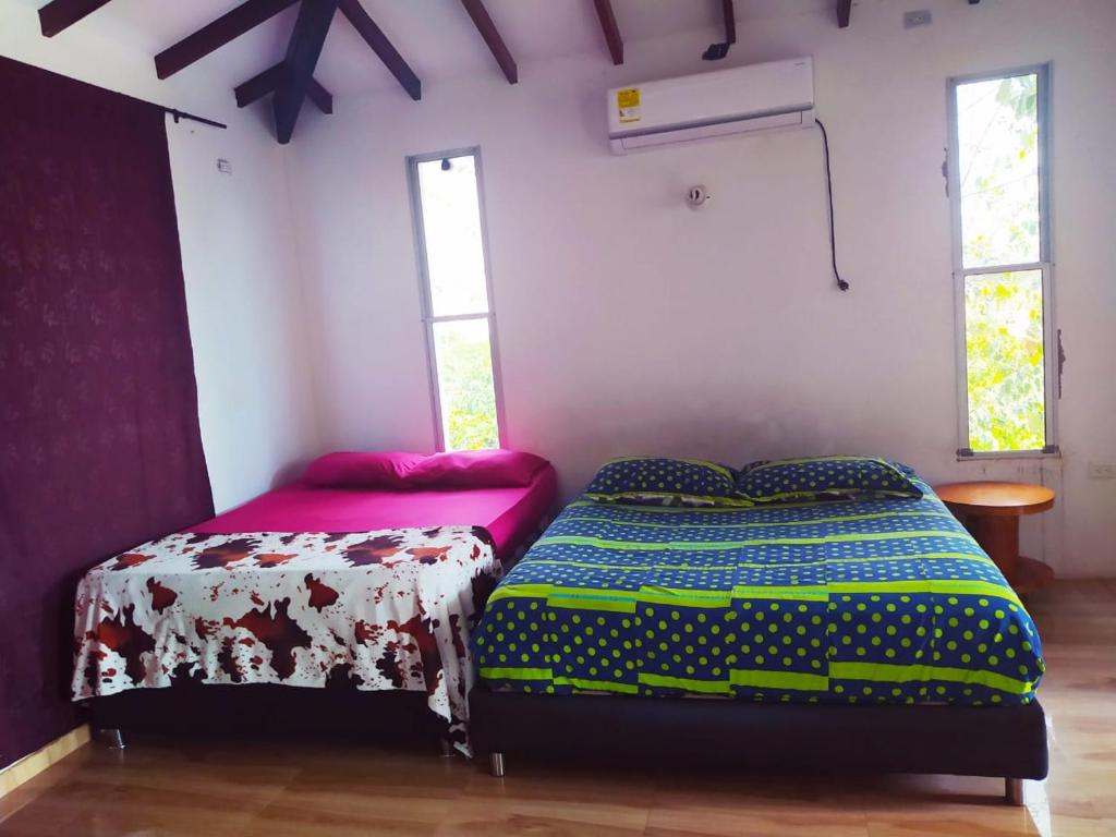 1 dormitorio con 2 camas, mesa y 2 ventanas en cabaña Milan, en Aguachica