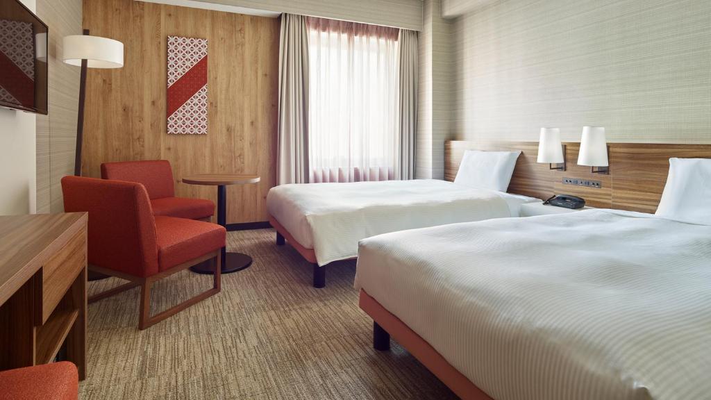 a hotel room with two beds and a chair at Mitsui Garden Hotel Kumamoto in Kumamoto