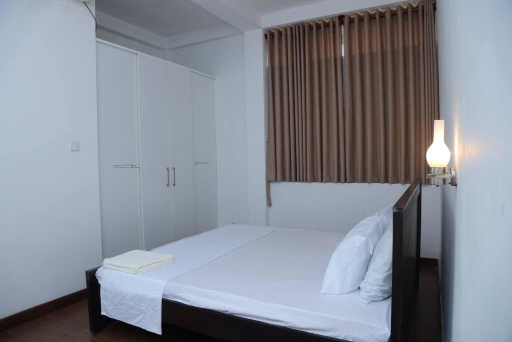 um quarto com uma cama com lençóis brancos e um candeeiro em The Paddy em Kottawa