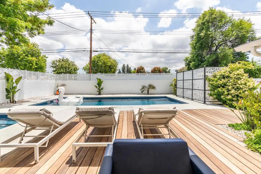a backyard with a swimming pool and a deck with chairs at New luxury entertaining house with Pool Spa Sauna Tesla charger Pets in Los Angeles