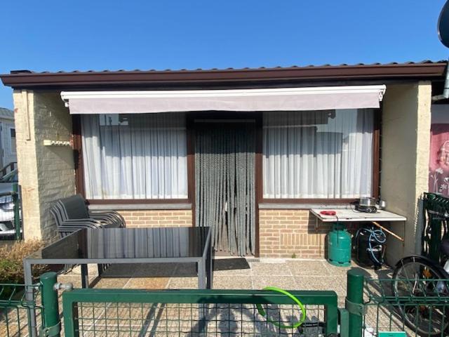 a patio with a table and a bench in front of a house at Camping Esmeralda in De Haan