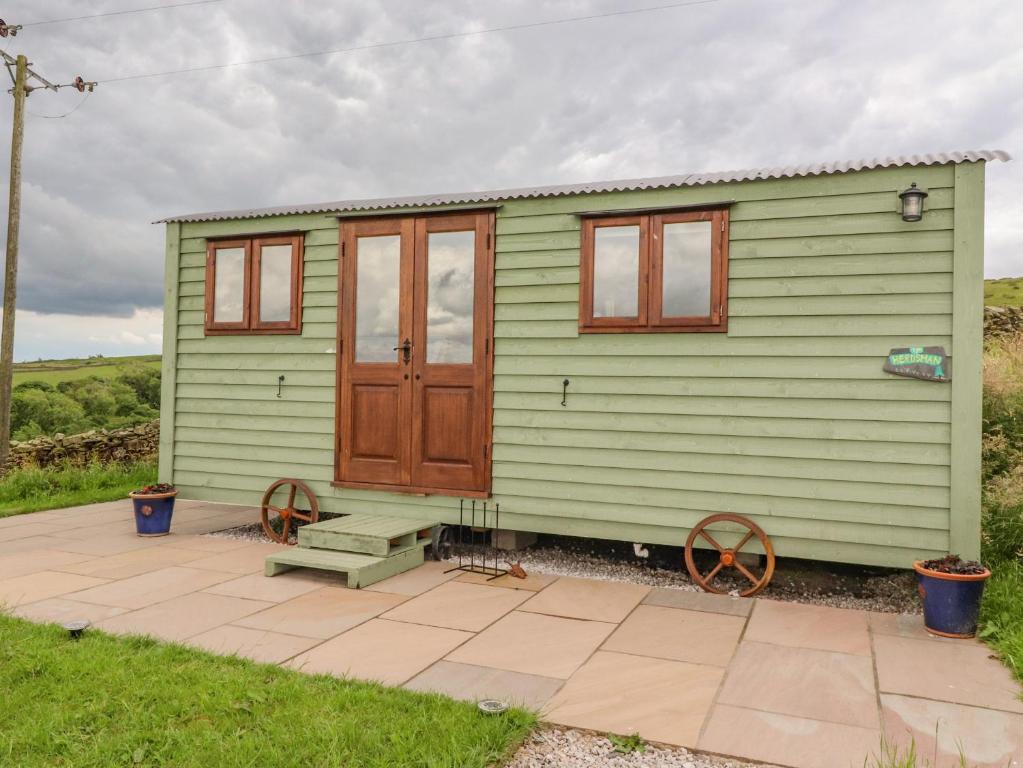 uma pequena casa verde com uma porta de madeira e um banco em The Herdsman Luxury Shepherds Hut em Barnoldswick