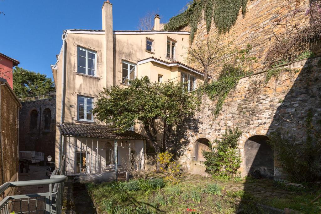 un vieux bâtiment en pierre avec un arbre en face de lui dans l'établissement Les jardins du Gourguillon, à Lyon