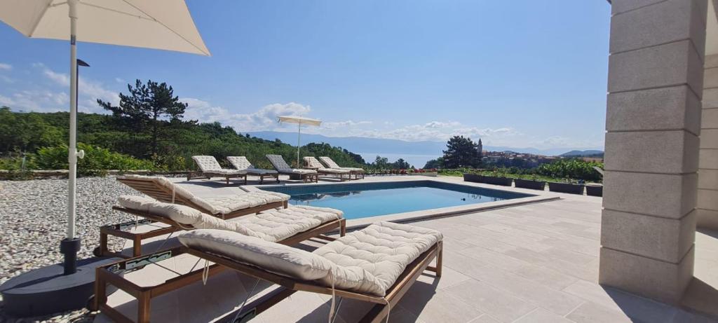 a swimming pool with lounge chairs and an umbrella at Apartmani Mariosa in Vrbnik