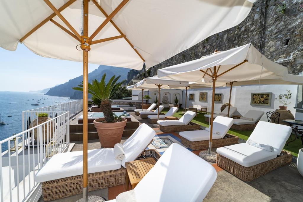 a patio with white chairs and umbrellas and the ocean at Villa Nina in Positano