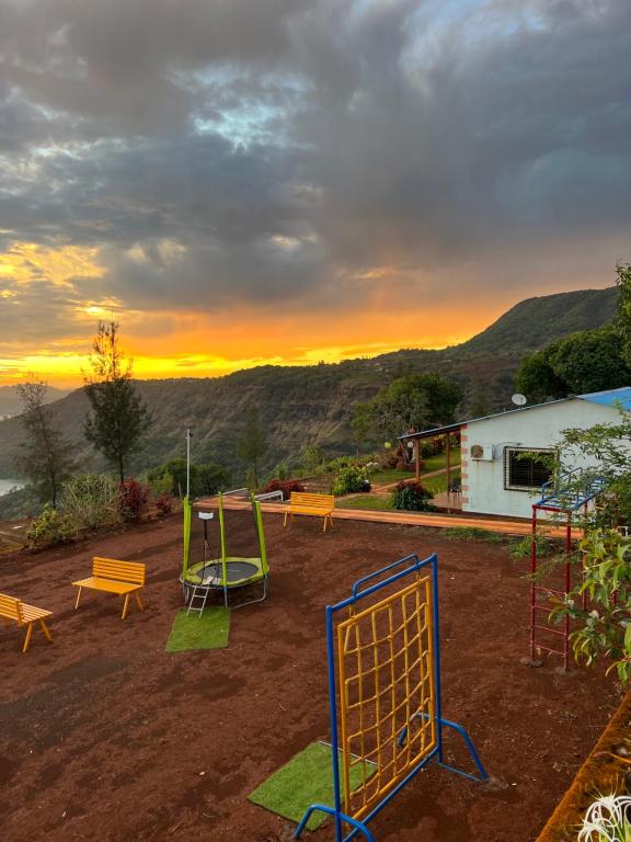a playground with benches and a sunset in the background at Heavens Edge Resort in Mahabaleshwar