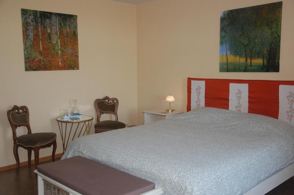 a bedroom with a bed with chairs and paintings on the wall at Le Buisson B&amp;B in Gouvy