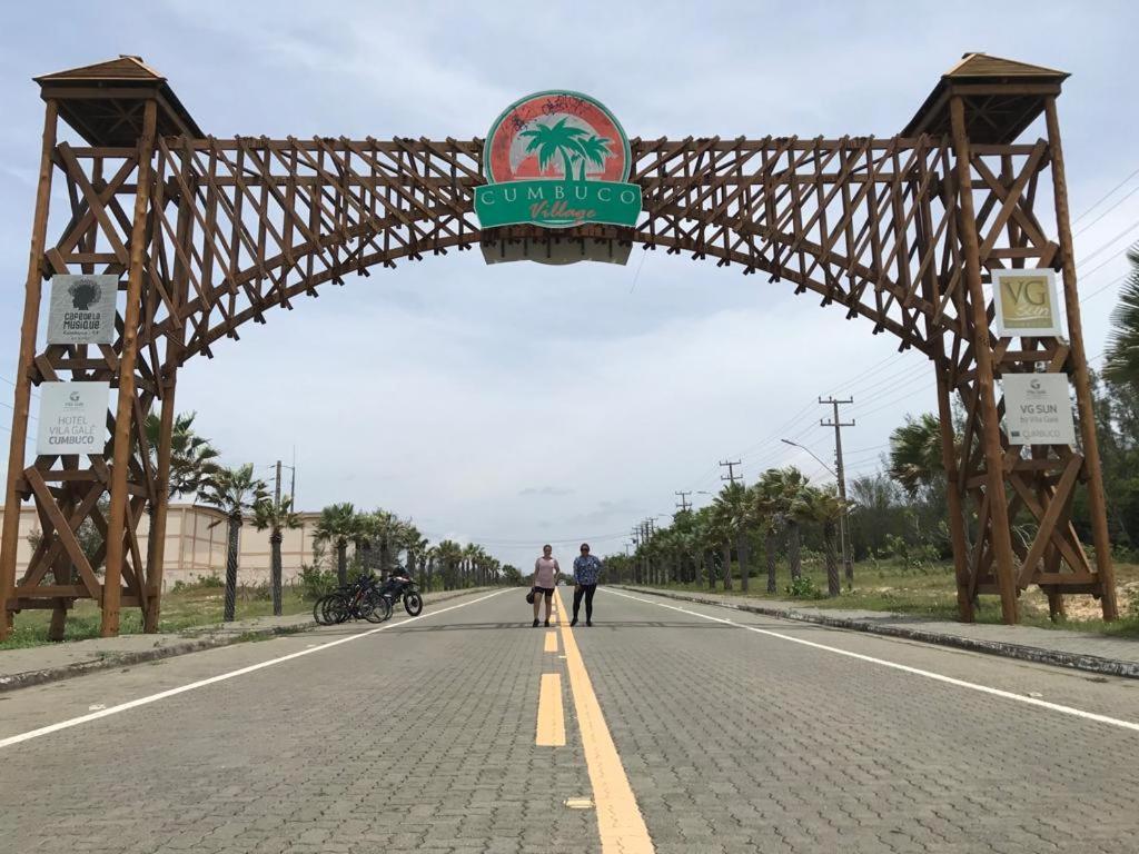 two people walking down a road under a wooden archway at Cumbuco Ap VGSUN 402 in Cumbuco