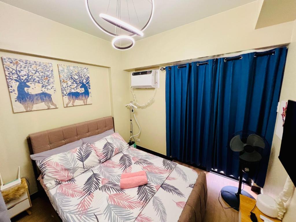 a bedroom with a bed and a window with blue curtains at Calathea Place by DMCI in Paranaque in Manila